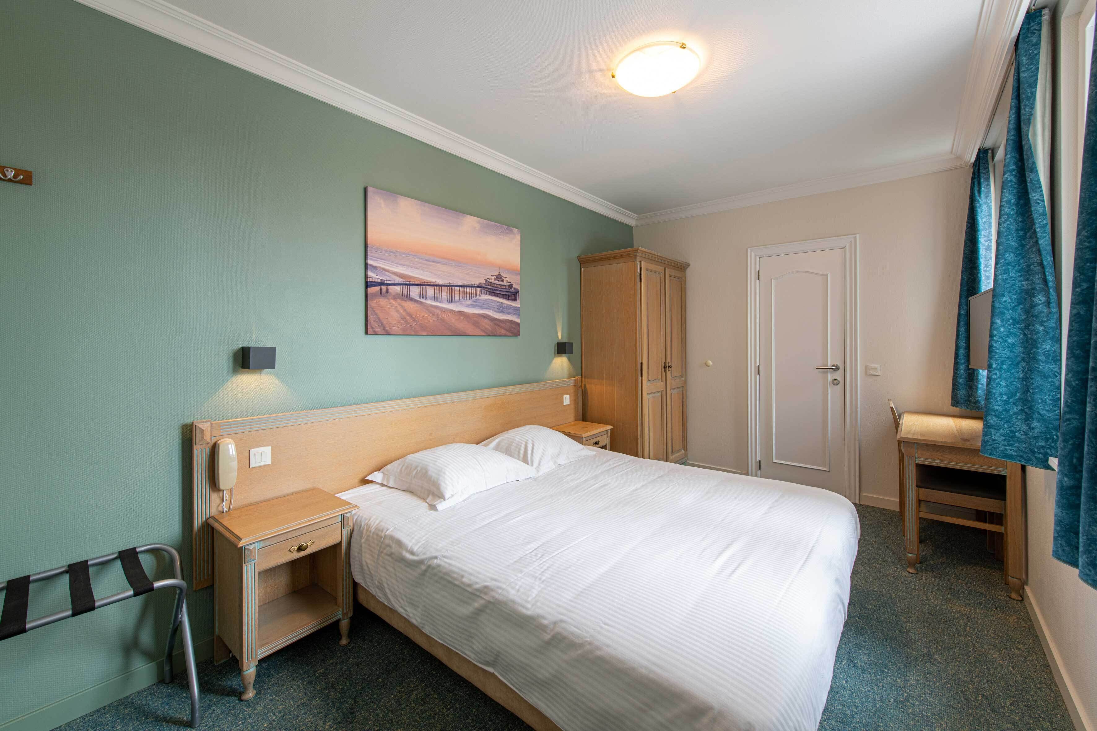 Une chambre d’hôtel comprenant un lit, une table de chevet, une armoire en bois, un bureau et une chaise.