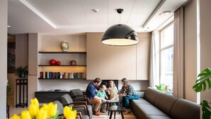 Un salon moderne comprenant un canapé, des fauteuils, une table basse et un grand luminaire suspendu. On y trouve également des étagères remplies de livres et d’objets décoratifs.