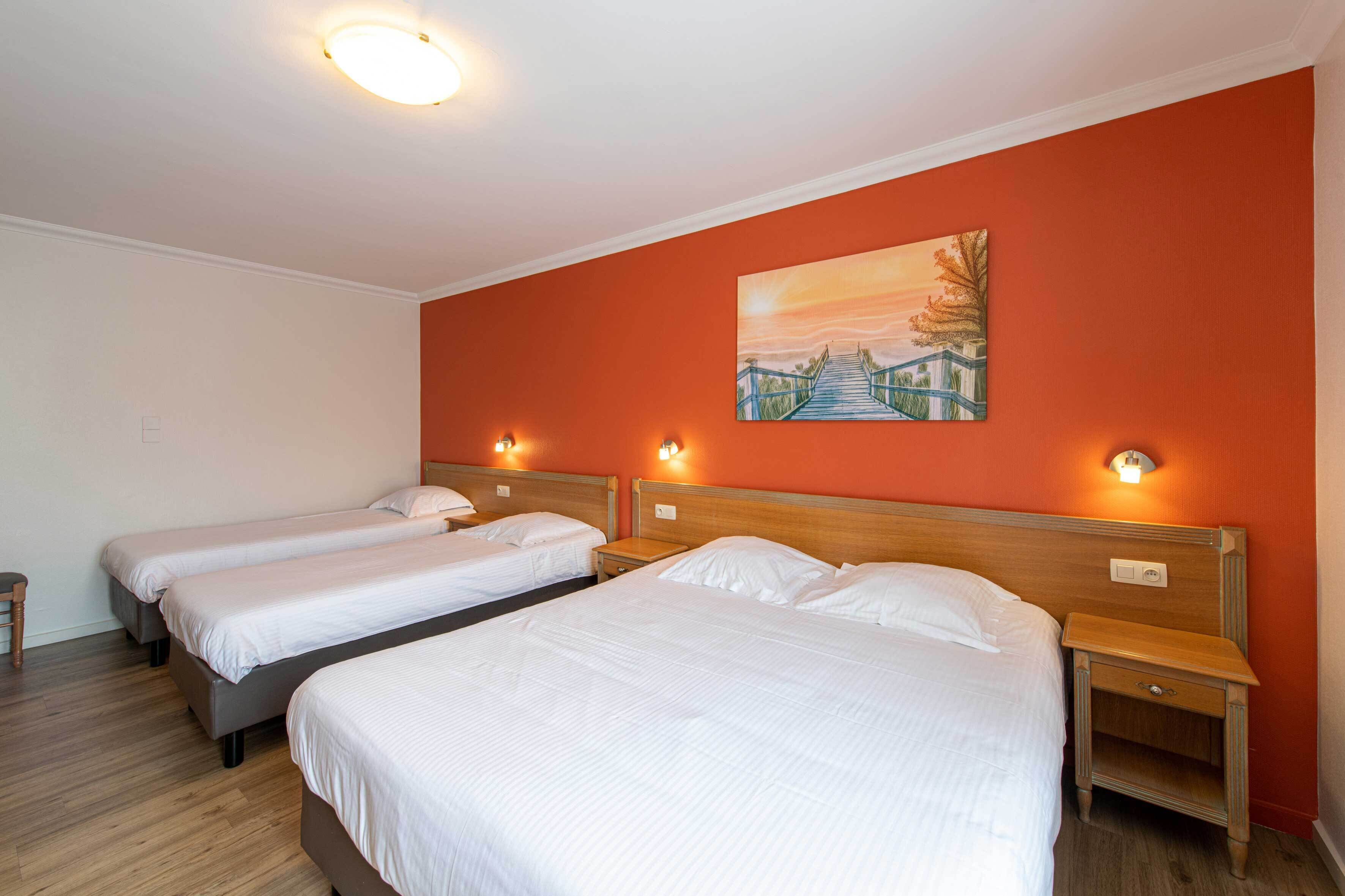 Een hotelkamer met drie enkele bedden, houten hoofdeinden en nachtkastjes met lampen.