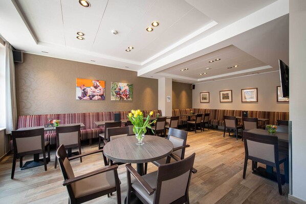 A spacious dining area with round tables and booths, a large wall with framed artwork, and a modern ceiling design.
