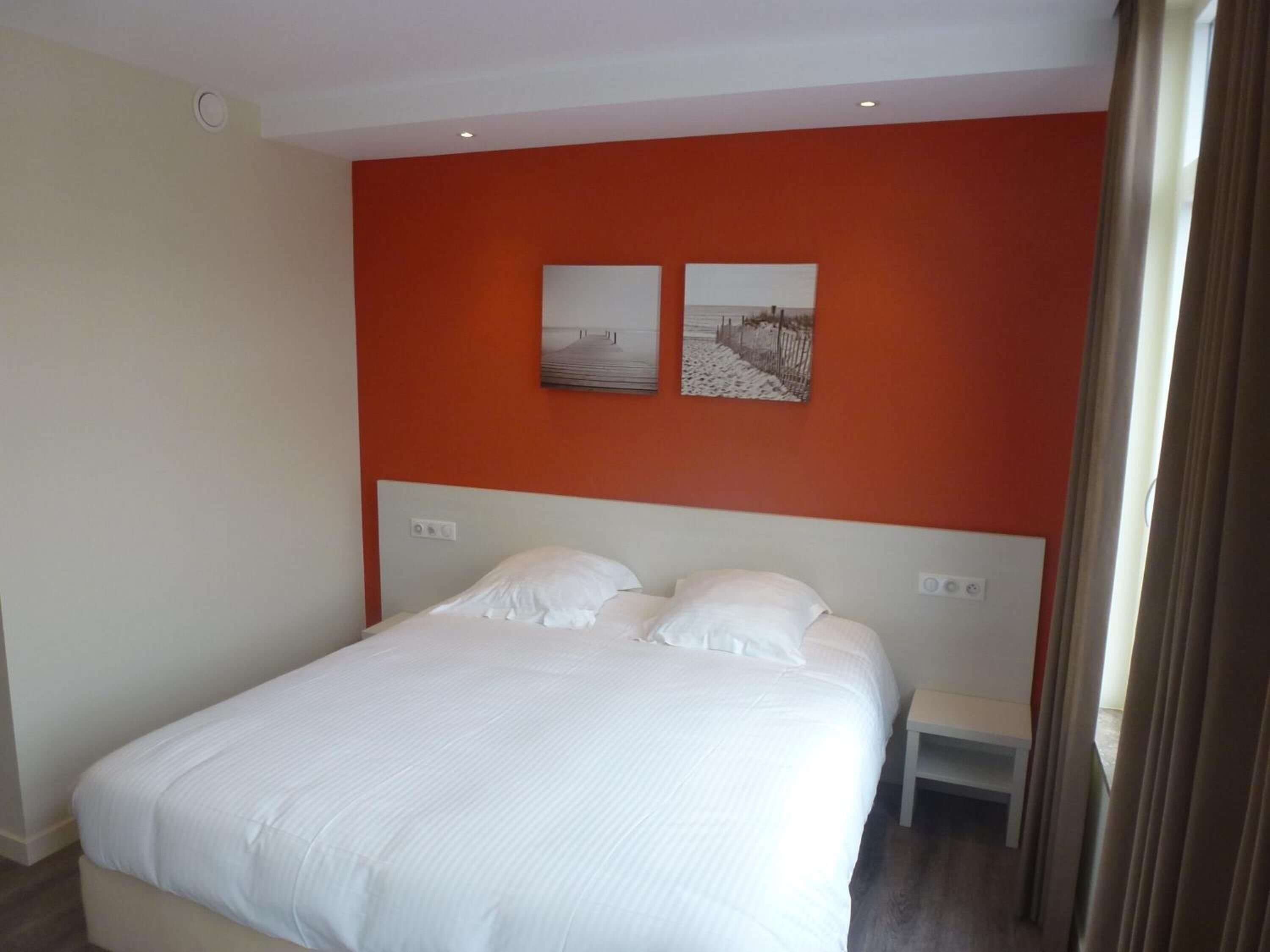 Una habitación de hotel con una cama grande, dos mesitas de noche y dos cuadros colgados en la pared.