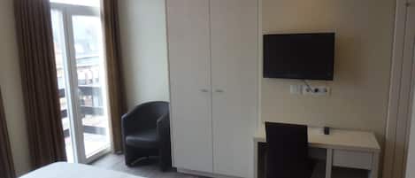 Una habitación de hotel con cama, escritorio, silla, televisor y armario.