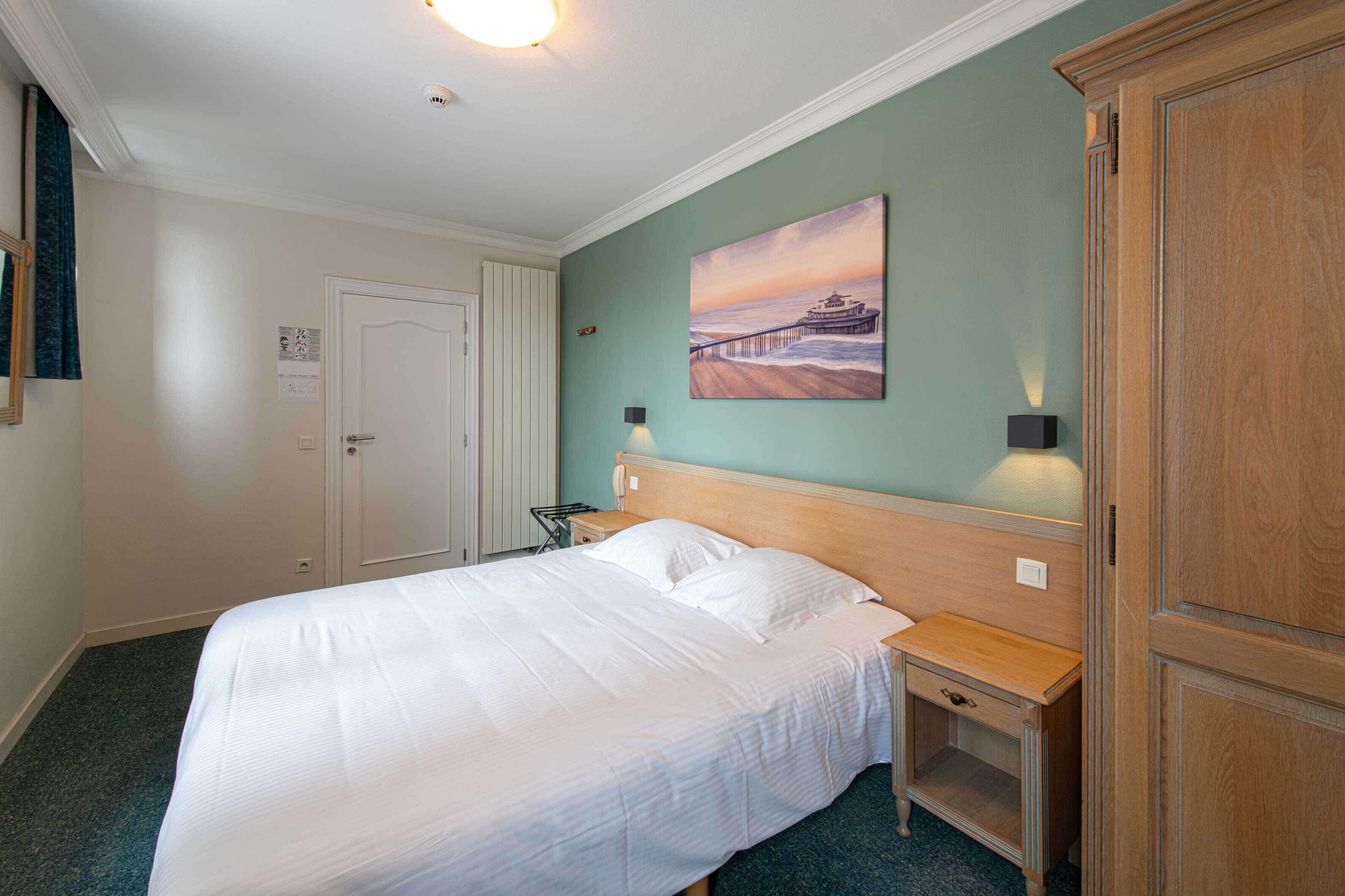 Ein Hotelzimmer mit einem großen Bett, einem Nachttisch, einem Holzschrank, einem Bild an der Wand und einer Lampe.