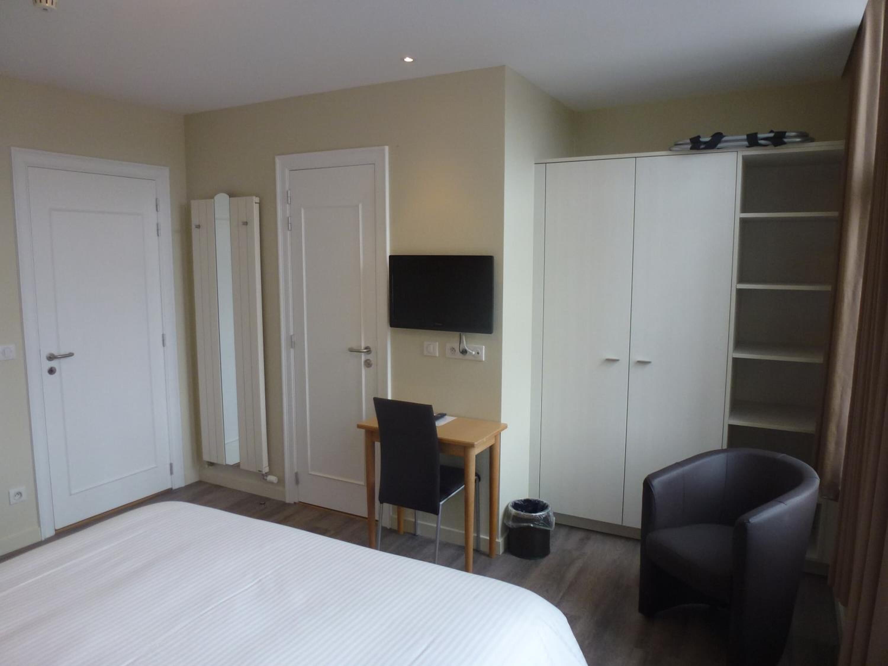 A hotel room with a bed, a desk, a chair, a TV, and a wardrobe.