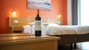Une bouteille de vin du château Pascaud et deux verres sur une table en bois, dans une chambre d’hôtel avec un lit et un tableau au mur.