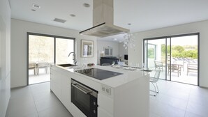 A modern kitchen with a central island, large windows, and a dining area with outdoor seating. - Las Colinas Golf & Country Club (Orihuela)