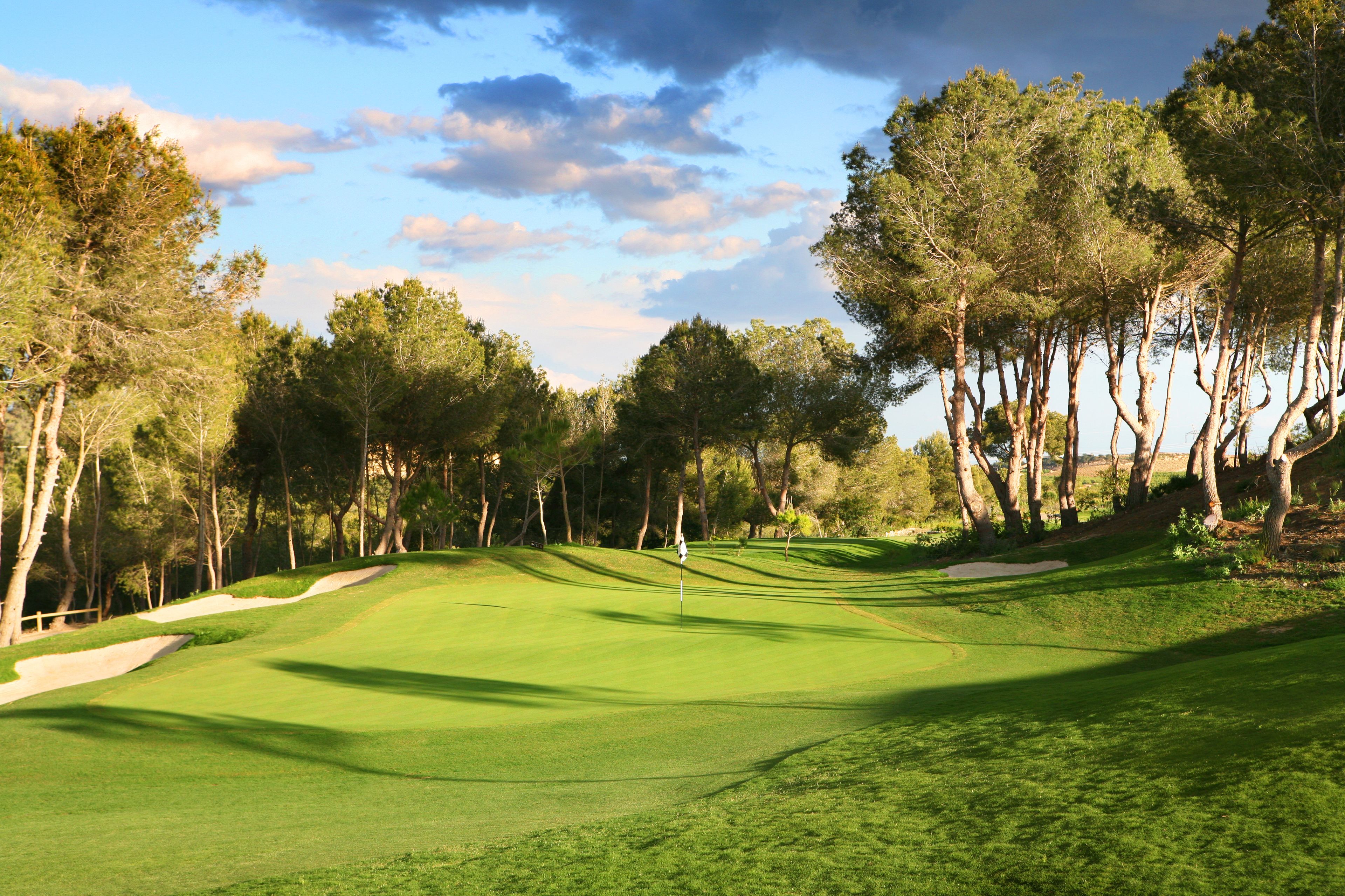 Un campo de golf con búnkeres de arena, un marcador de bandera y árboles.