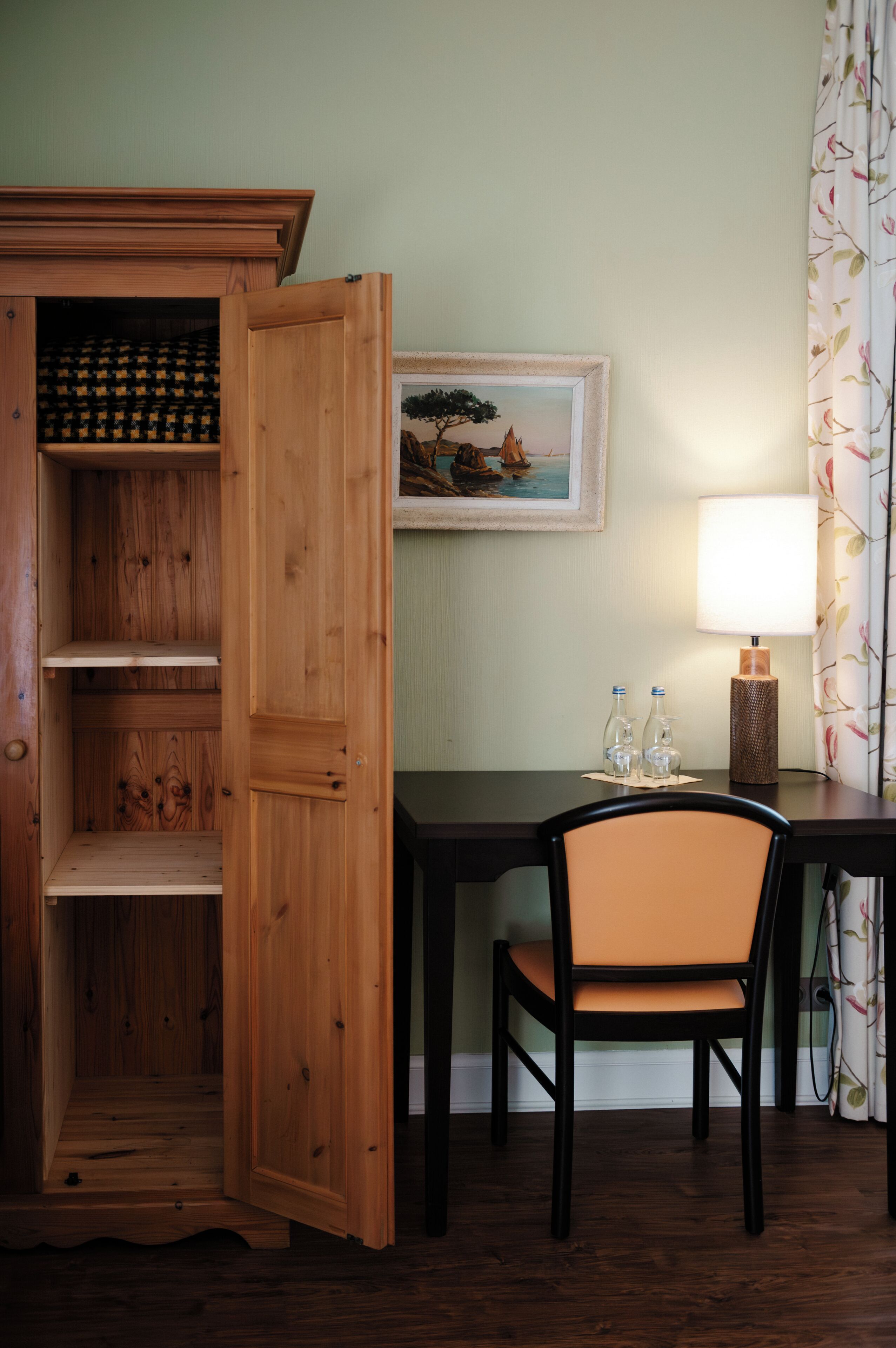 Un meuble en bois avec des étagères, un tableau encadré accroché au mur, une table avec une chaise et une lampe.