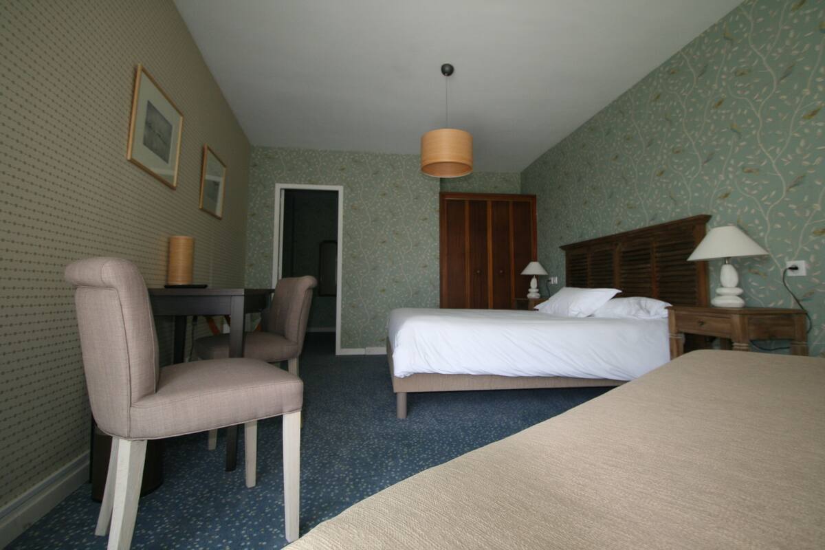 A hotel room with a bed, a desk with a chair, a wardrobe, and a lamp.