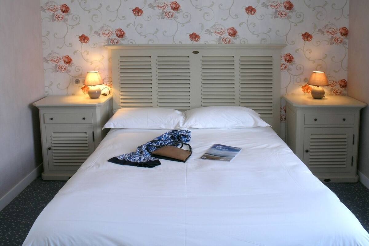 A neatly made bed with white linens, two bedside tables with lamps, and floral wallpaper.