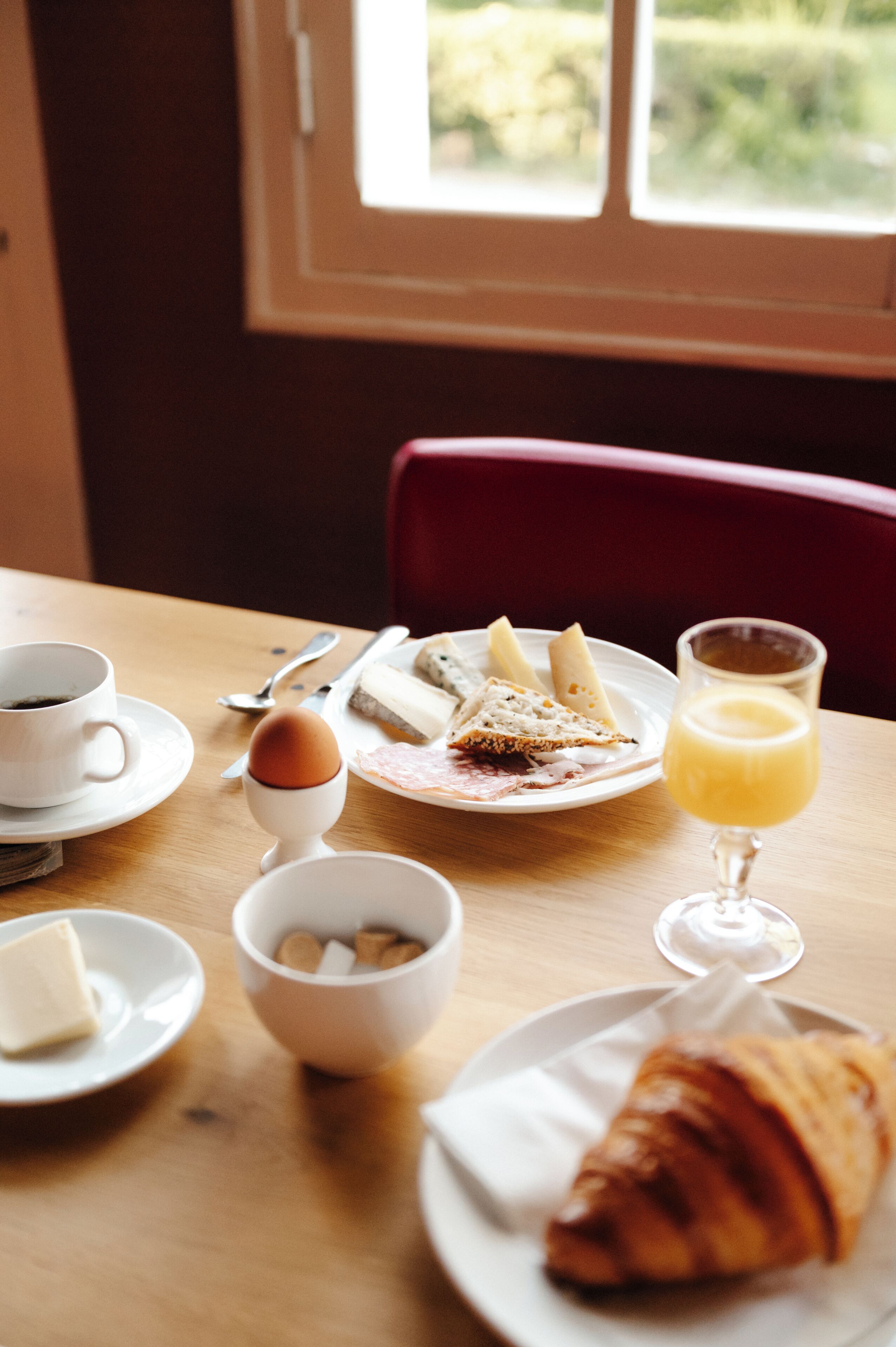 Ein Frühstückstisch mit einem Croissant, einem Glas Orangensaft, einem Teller mit einem Sandwich, einer Schüssel mit Eiern und einer Tasse Kaffee.