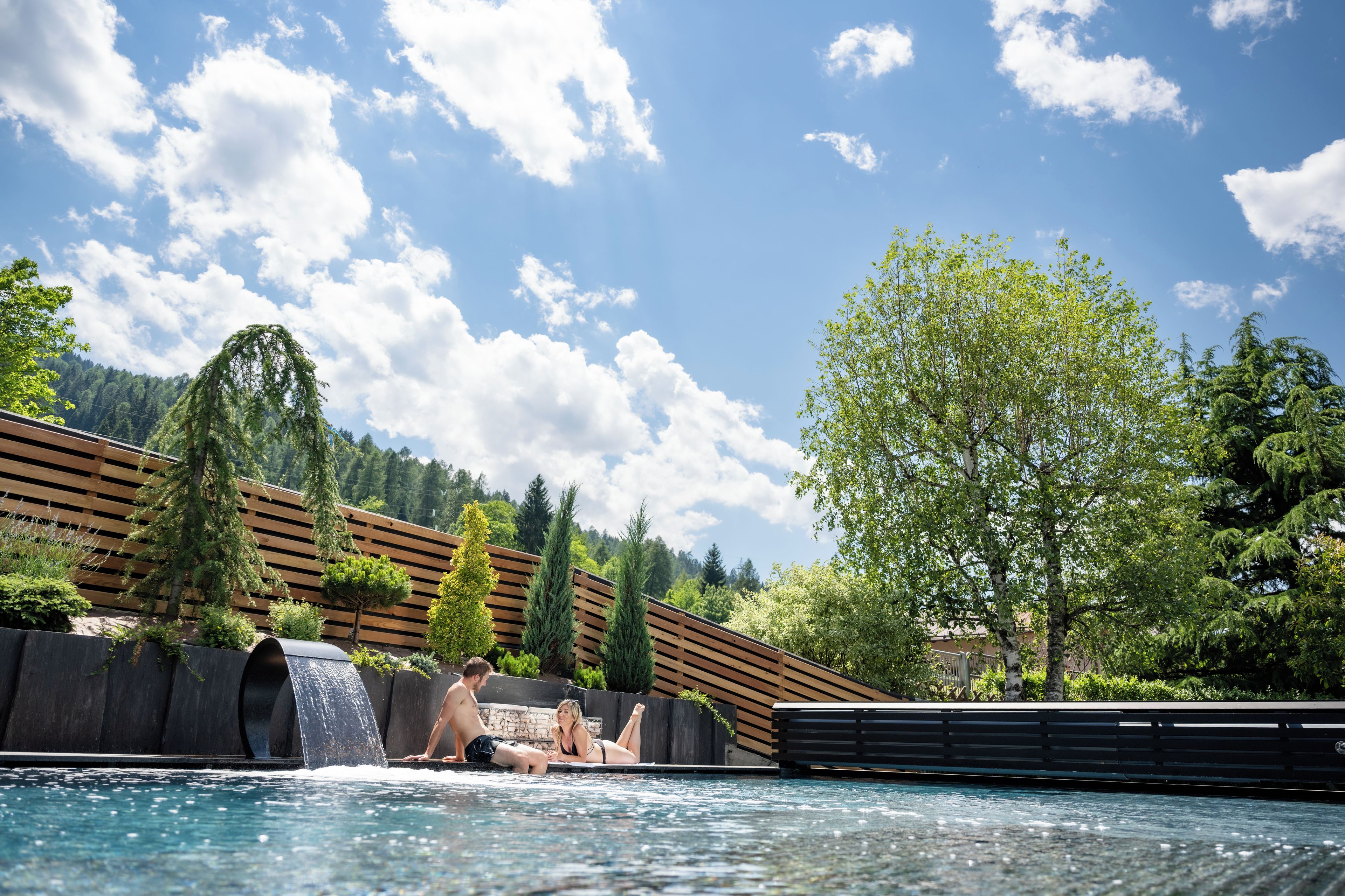 Una piscina con cascata, circondata da listelli di legno e vegetazione.