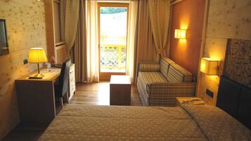 Una camera d'albergo con un letto, una scrivania con una lampada, un divano e vista su un balcone.