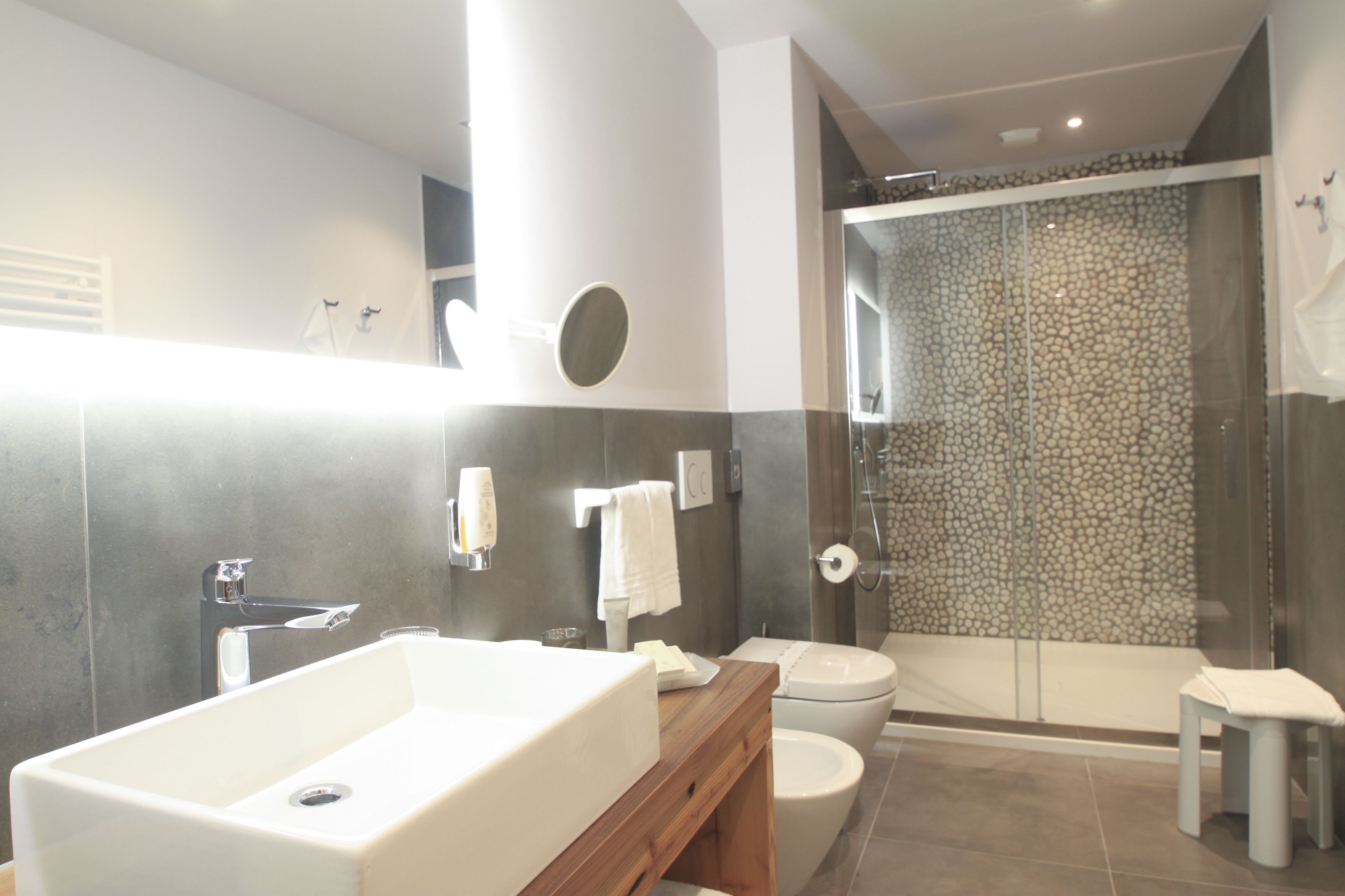 A modern bathroom with a large white bathtub, a toilet, and a shower area with a stone wall.