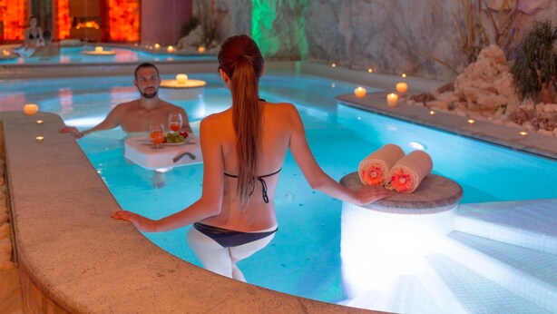 A pool area with a person holding towels and a fruit bowl, and another person in the background.
