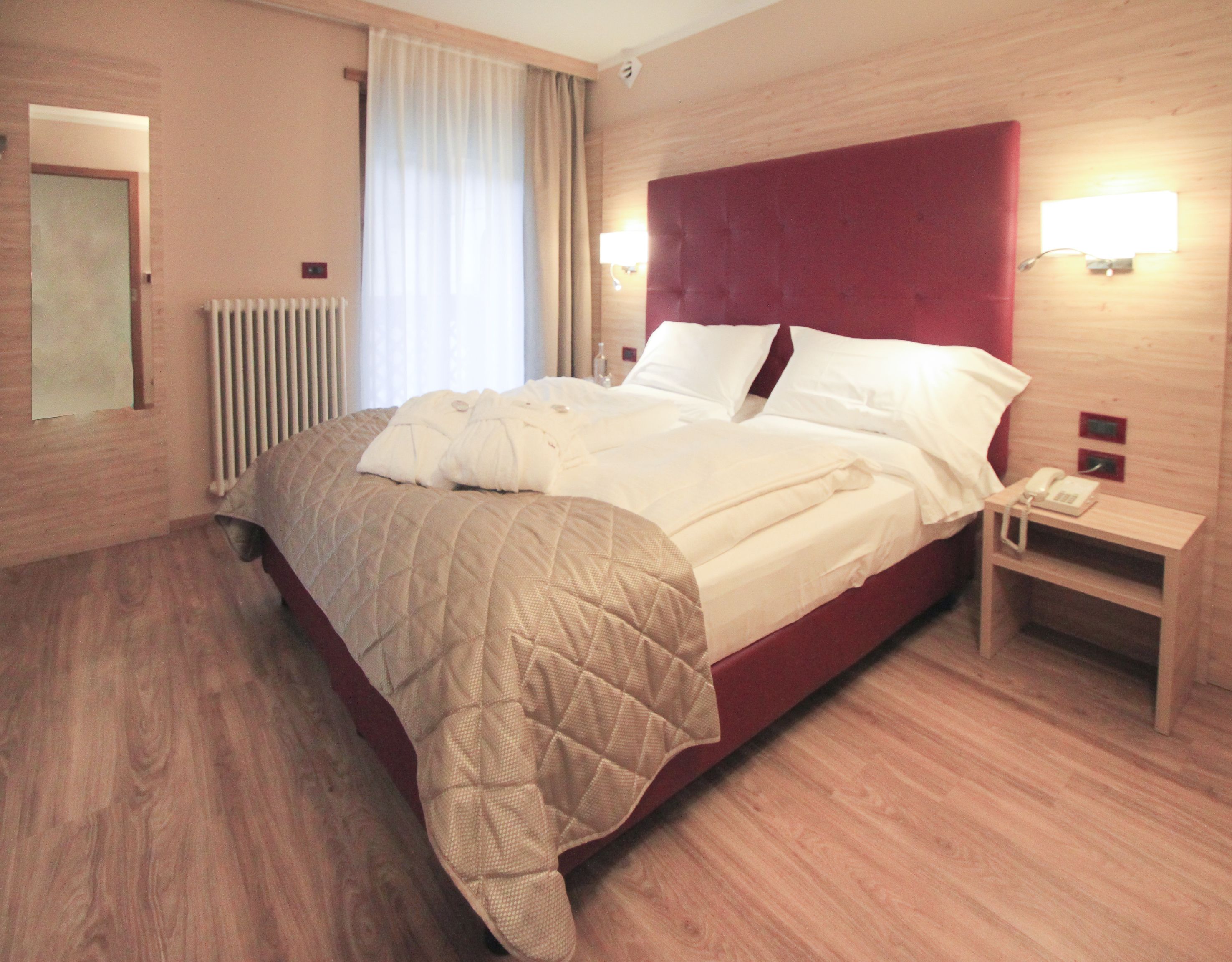 A hotel room with a large bed, a bedside table with a phone, and a radiator.