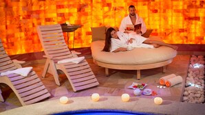 A spa area with a heated stone wall, a pool, and lounge chairs.