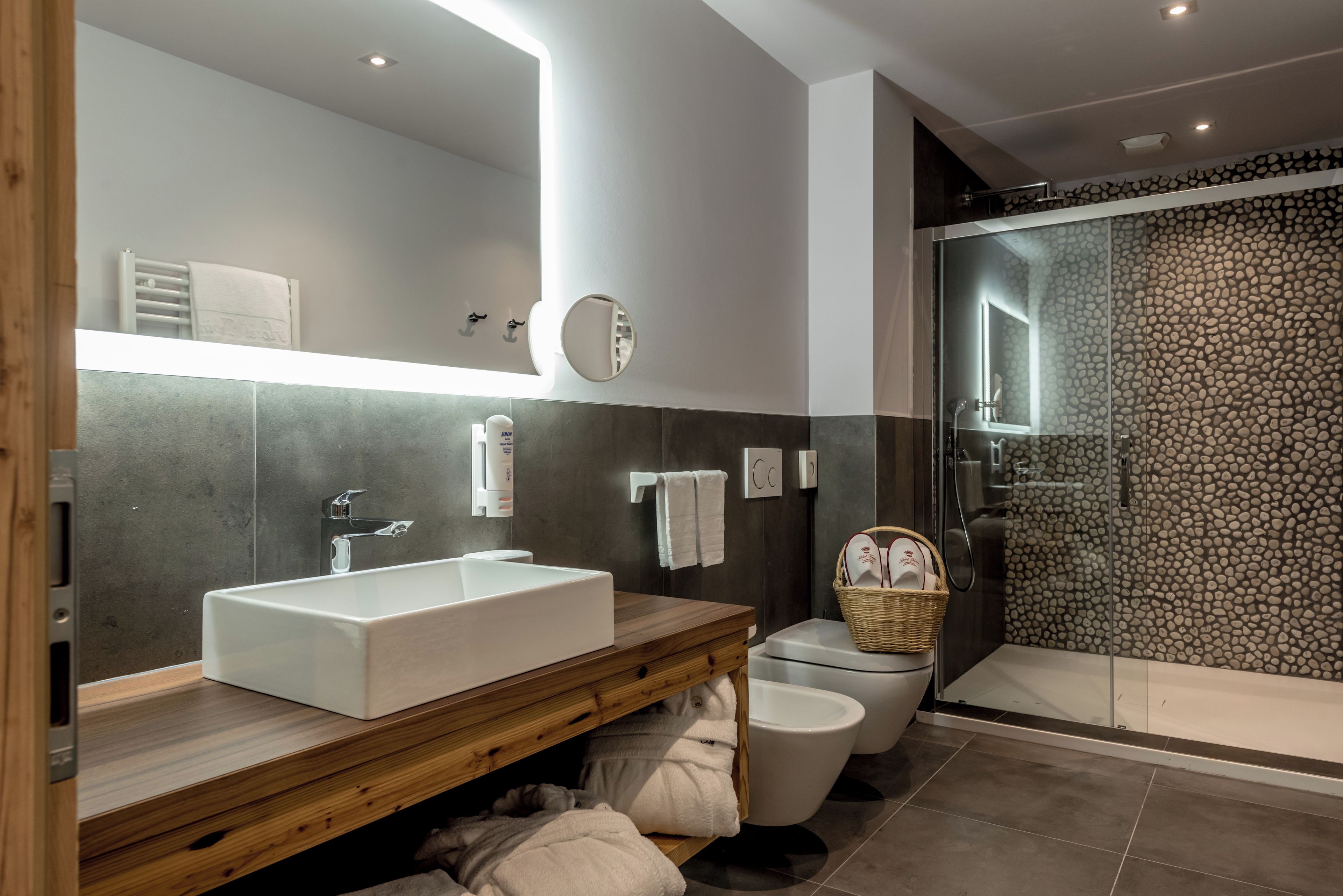 Un bagno moderno con un lavandino bianco di grandi dimensioni, uno specchio, un mobile bagno in legno, un WC e una cabina doccia in vetro.