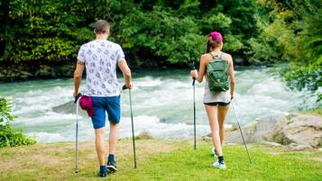 Dos personas caminando con bastones de trekking cerca de un río, rodeadas de vegetación.