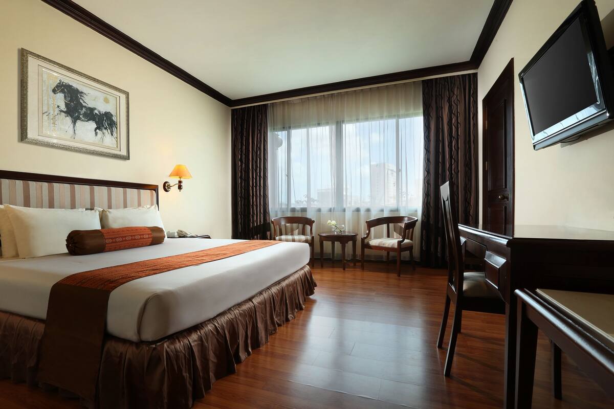 Habitación de hotel con una cama grande, un escritorio, una silla, un televisor y una ventana con cortinas.
