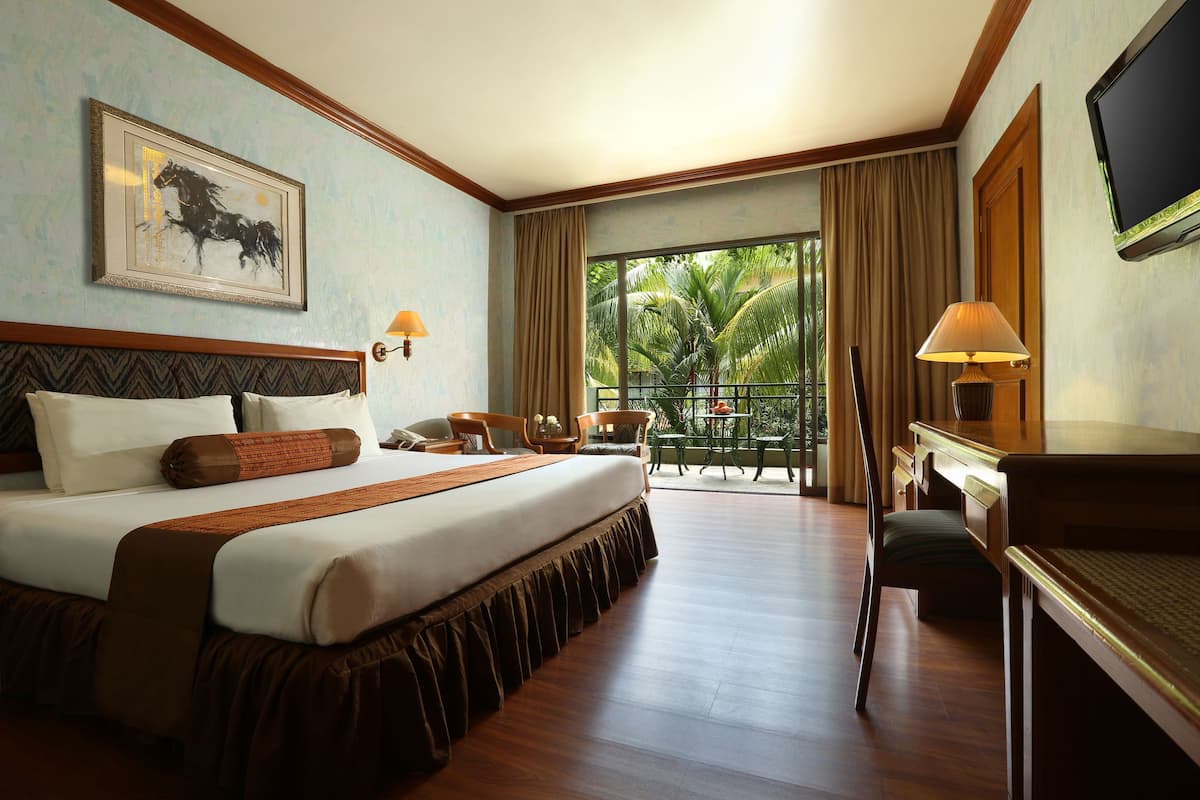 Habitación de hotel con una cama grande, un escritorio, una silla, un televisor y un balcón con vistas a palmeras.