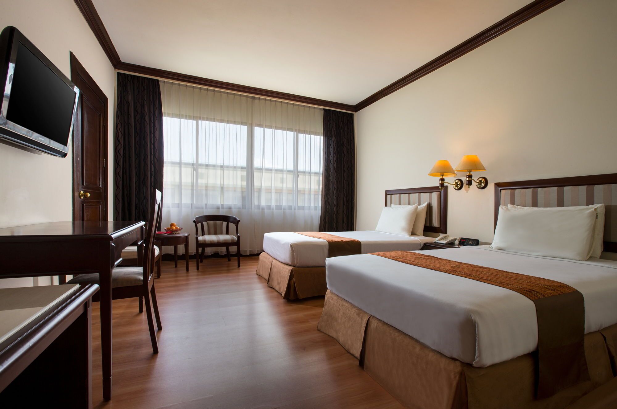 A hotel room with two beds, a desk, a chair, a TV, and a window with curtains.