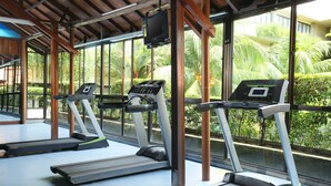 A gym with treadmills and a TV screen, large windows, and a view of greenery outside. - Goodway Hotel Batam (Batam)