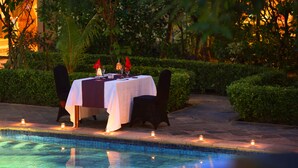 An outdoor dining area with a table set for two, surrounded by a pool and greenery. - Goodway Hotel Batam (Batam)