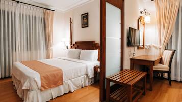 Una habitación de hotel con una cama grande, un banco de madera, un escritorio con una silla, un televisor y un espejo.
