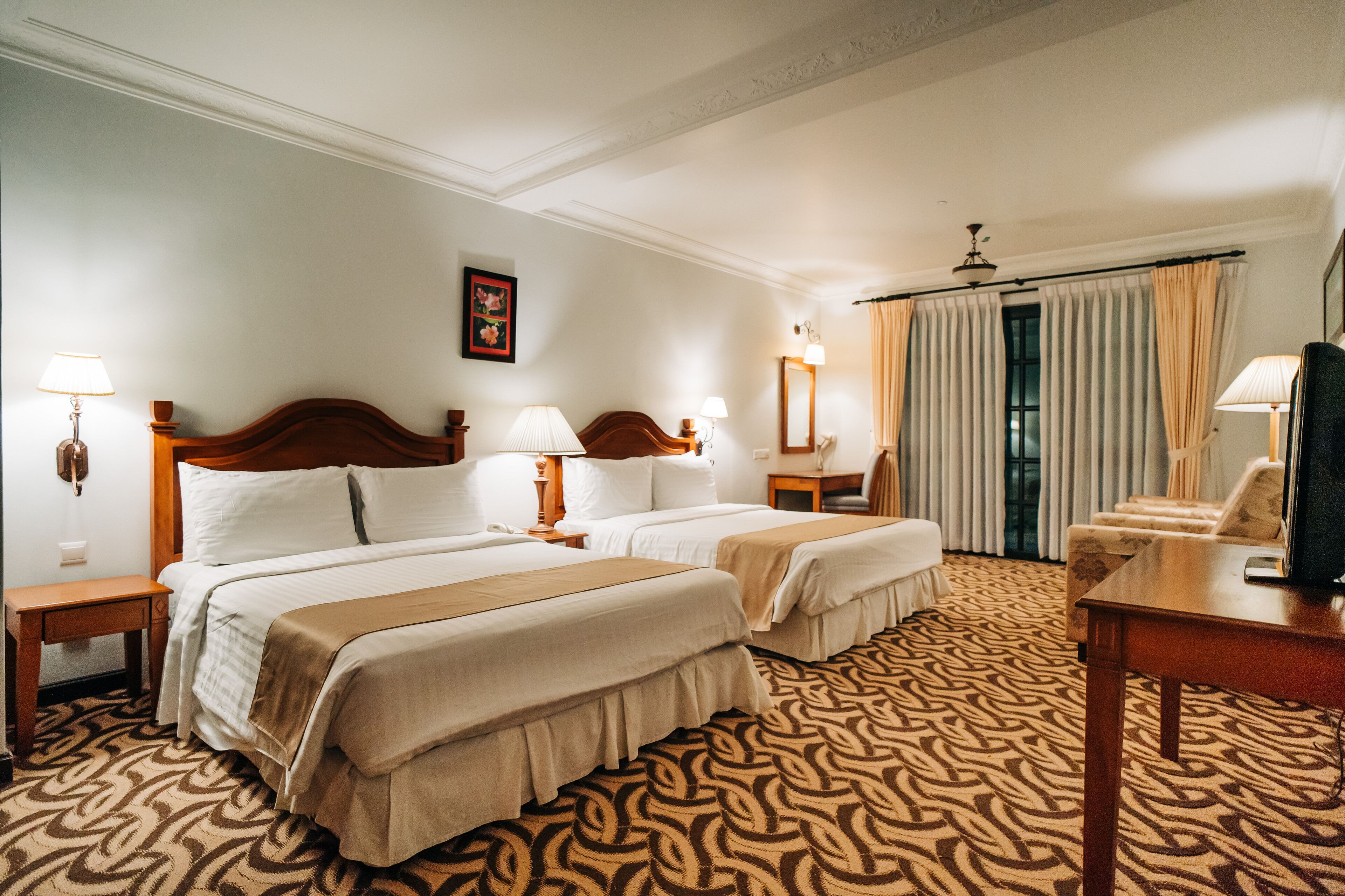 A hotel room with two beds, a desk, a chair, and a television.