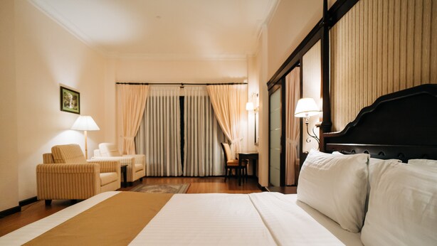 A hotel room with a large bed, a sitting area with a chair and a table, and a piano. - Hotel De'La Ferns, Cameron Highlands (Tanah Rata)