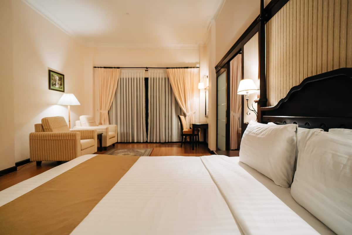 A hotel room with a large bed, a sitting area with a chair and a table, and a piano.