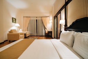 A hotel room with a large bed, a sitting area with a chair and a table, and a piano.