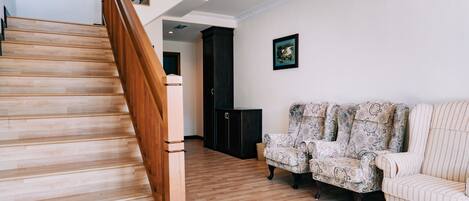 A staircase with wooden steps and a handrail, leading to a dark-colored room with patterned armchairs and a framed picture on the wall.