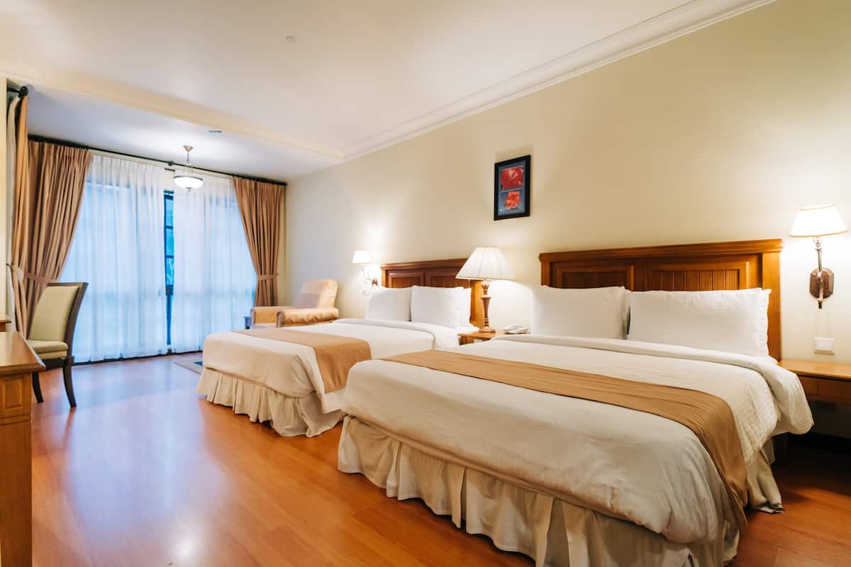 A hotel room with two beds, a chair, a desk, and a window with curtains.