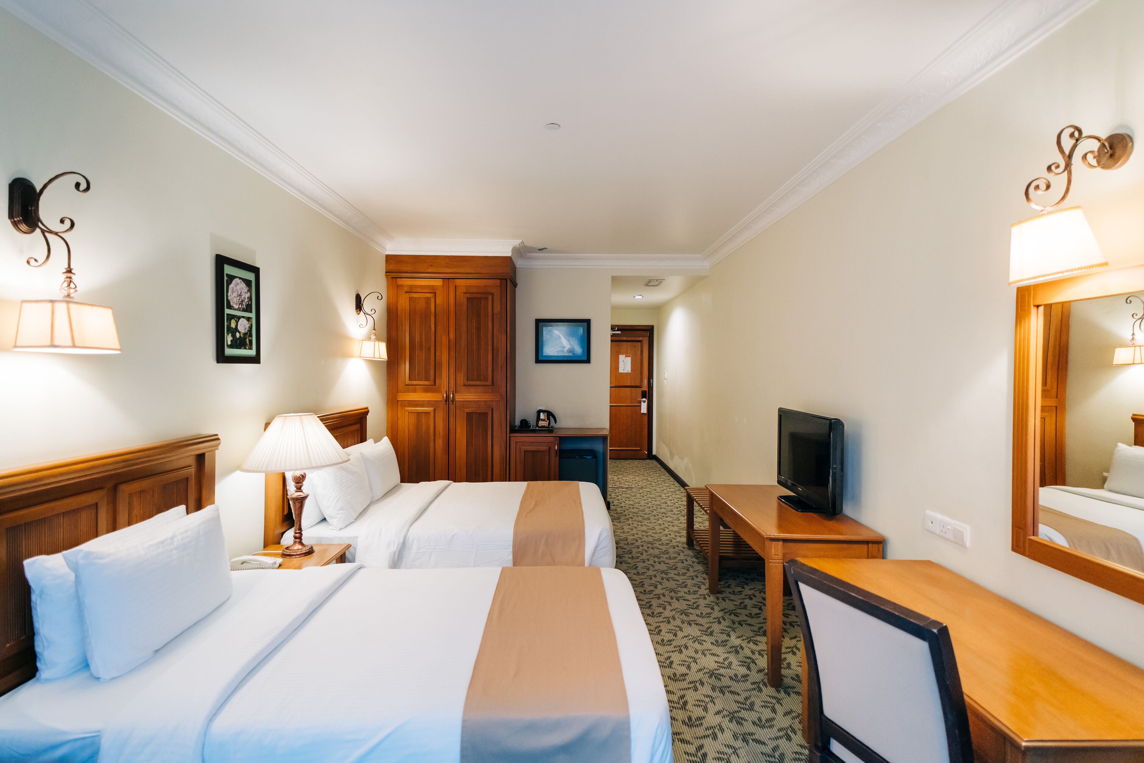 A hotel room with two beds, a desk, a television, and a mirror.