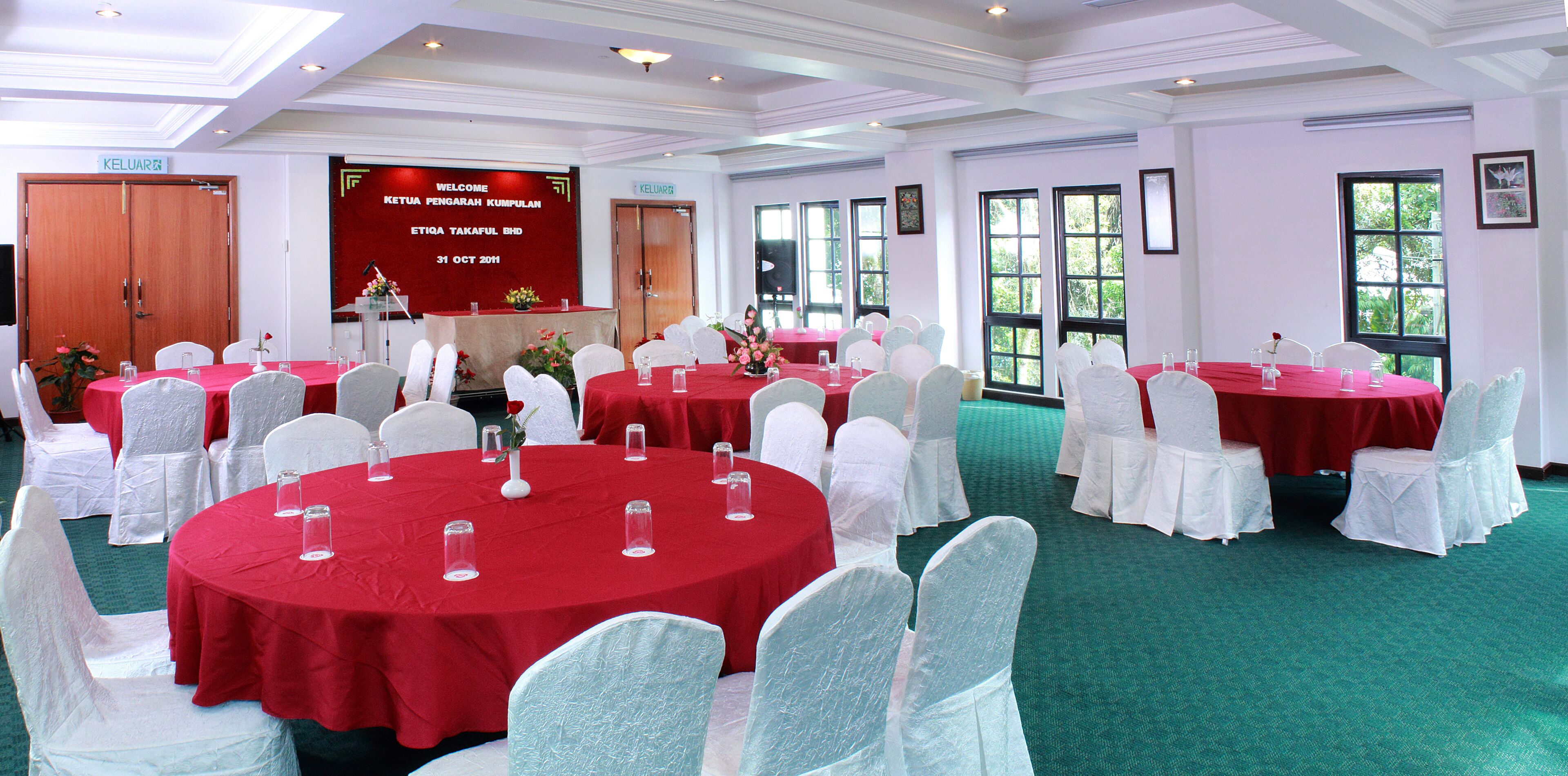 A conference room with round tables covered in red tablecloths, white chairs, and a large screen displaying a welcome message.