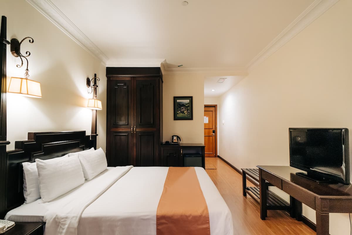 A hotel room with a bed, bedside lamps, a desk with a television, and a door leading to another room.