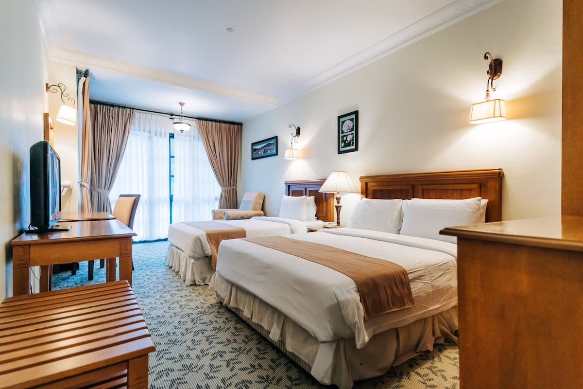 A hotel room with two beds, a desk, a chair, a television, and a window with curtains.