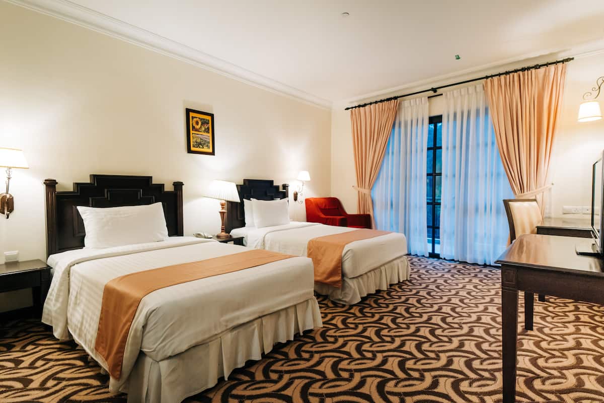 A hotel room with two beds, a red chair, a desk, and a patterned carpet.
