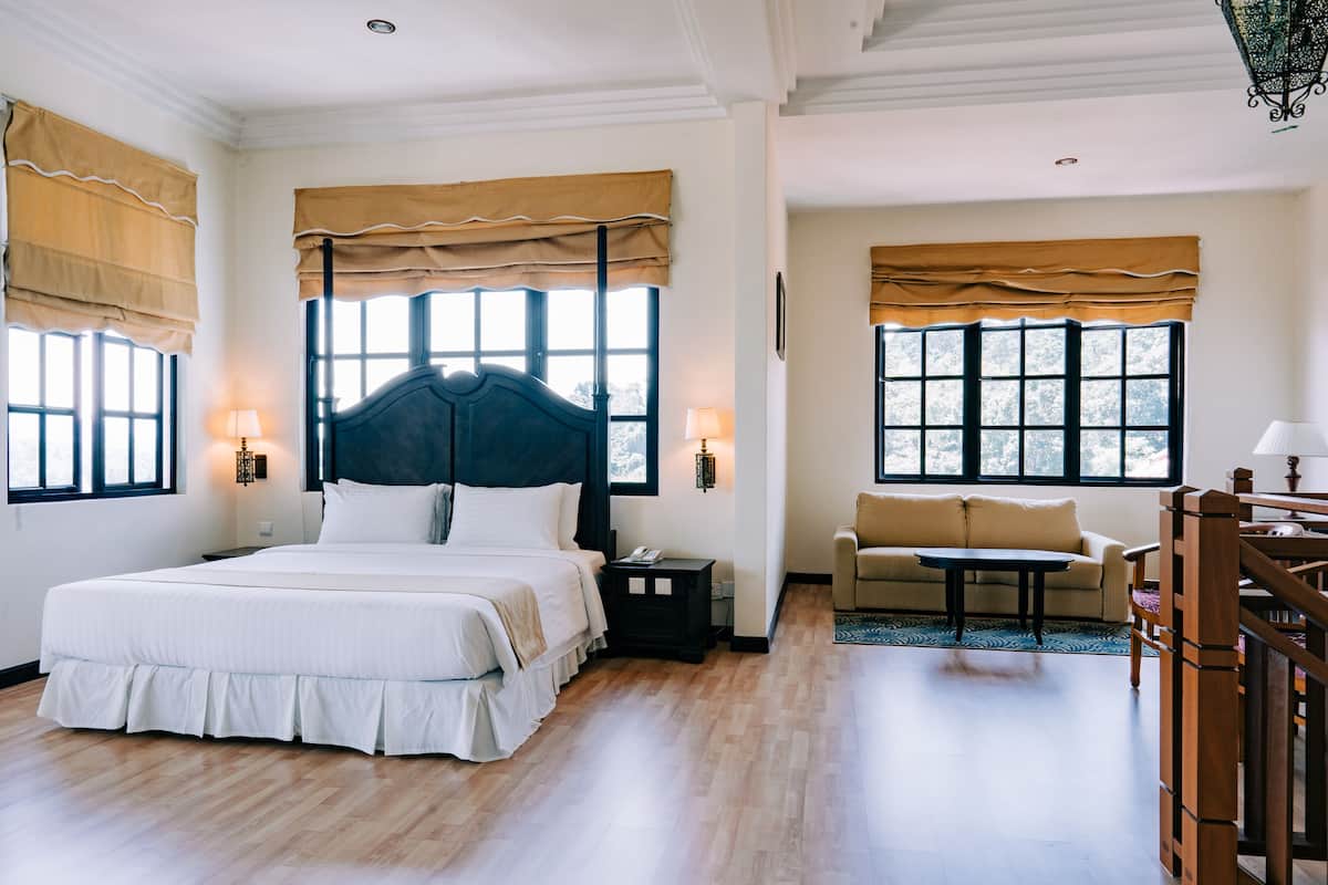 A bedroom with a large bed, two bedside tables, a nightstand, a sofa, and a small table.