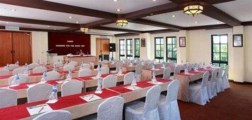 A conference room with rows of tables, chairs, and a stage with a speaker.