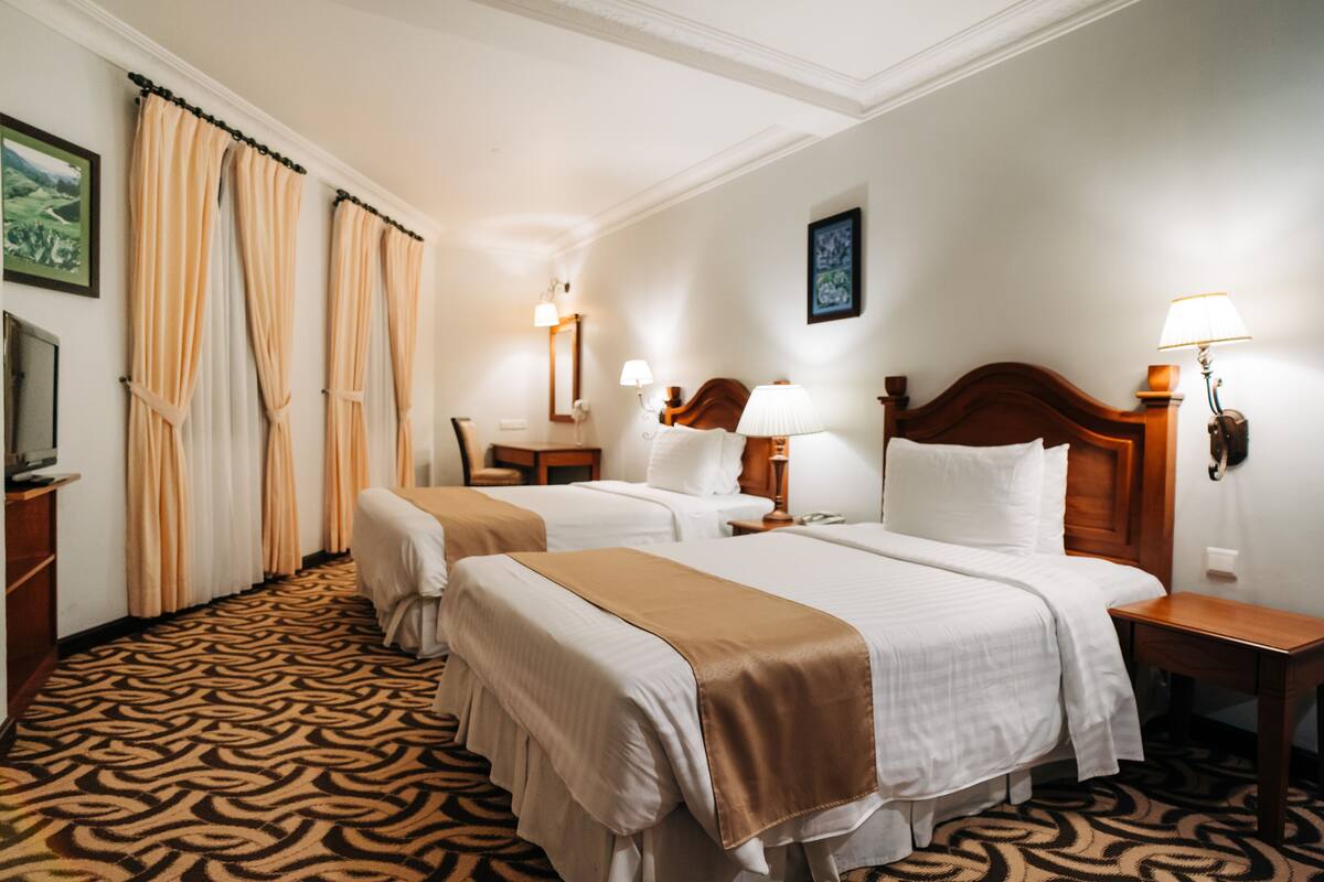 A hotel room with two beds, a patterned carpet, and a wooden headboard.