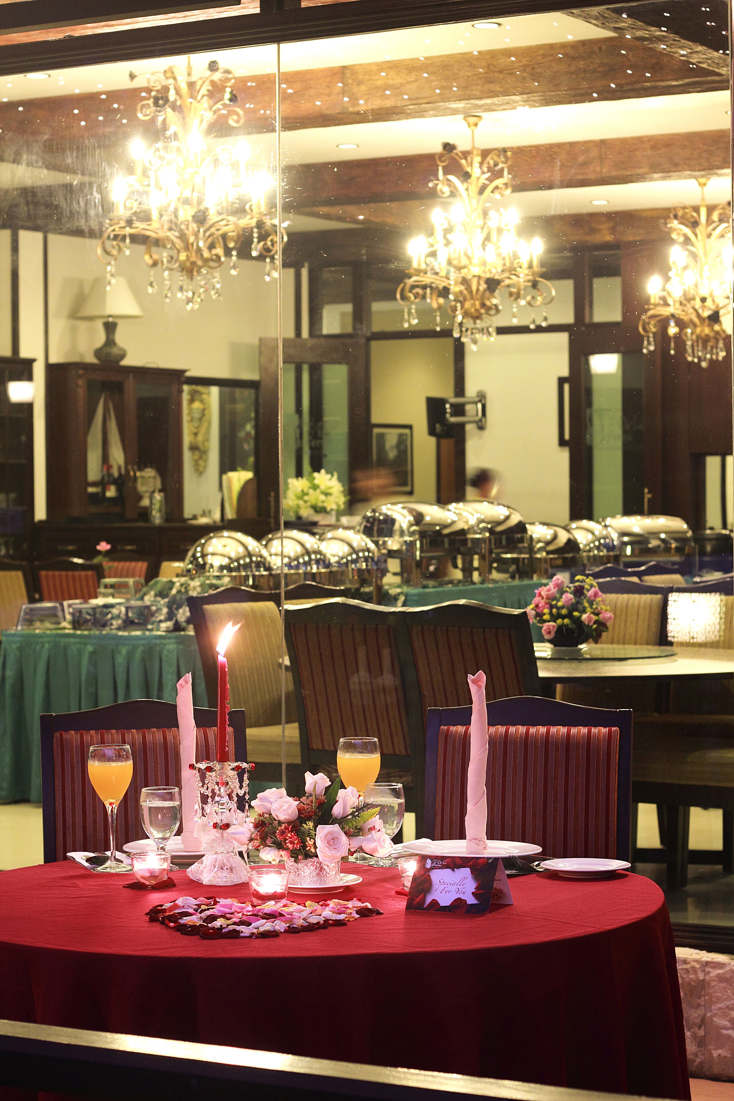 A dining area with a red tablecloth, candles, and a floral centerpiece.