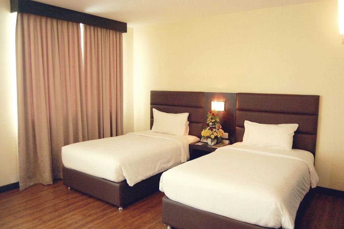 A hotel room with two beds, a nightstand with a lamp, and a window with curtains.