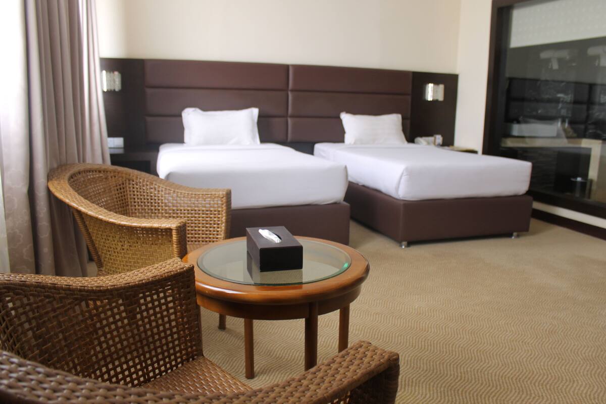 A hotel room with two beds, a glass table, and wicker chairs.
