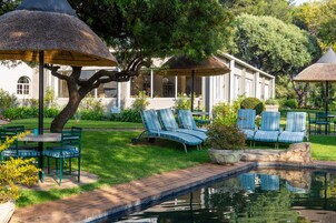 Un área junto a la piscina con sillones de descanso, sombrillas y un edificio al fondo.