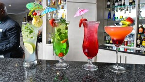 Drie cocktails op een bar met een barman op de achtergrond.