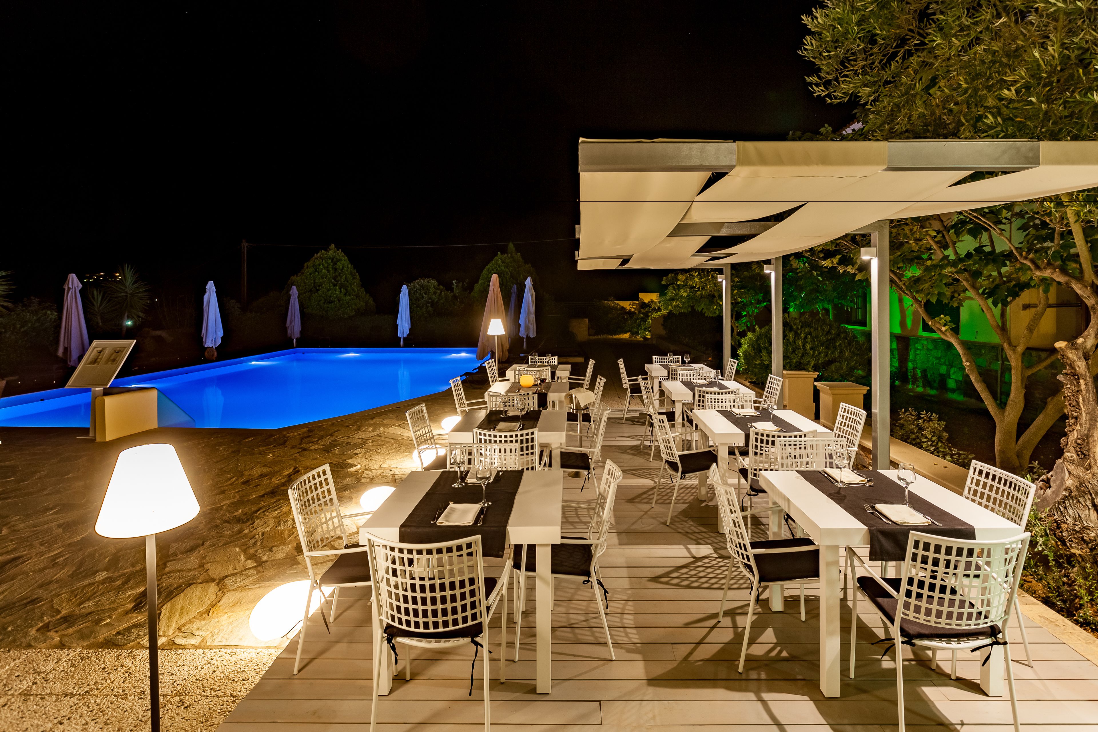 An outdoor dining area with tables and chairs, a pool, and umbrellas.