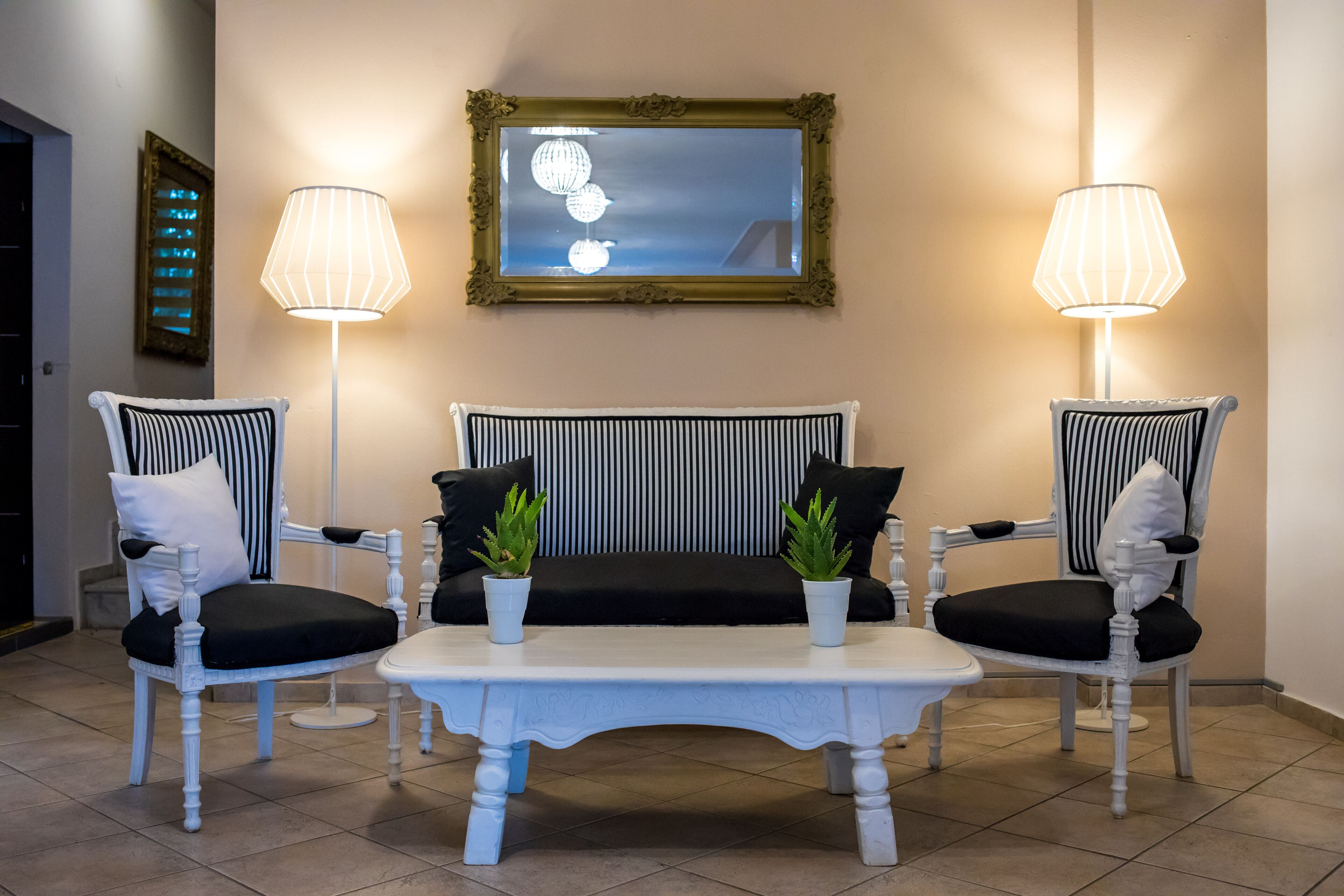 Uma área de estar com duas cadeiras brancas, uma mesa branca e duas luminárias de chão.